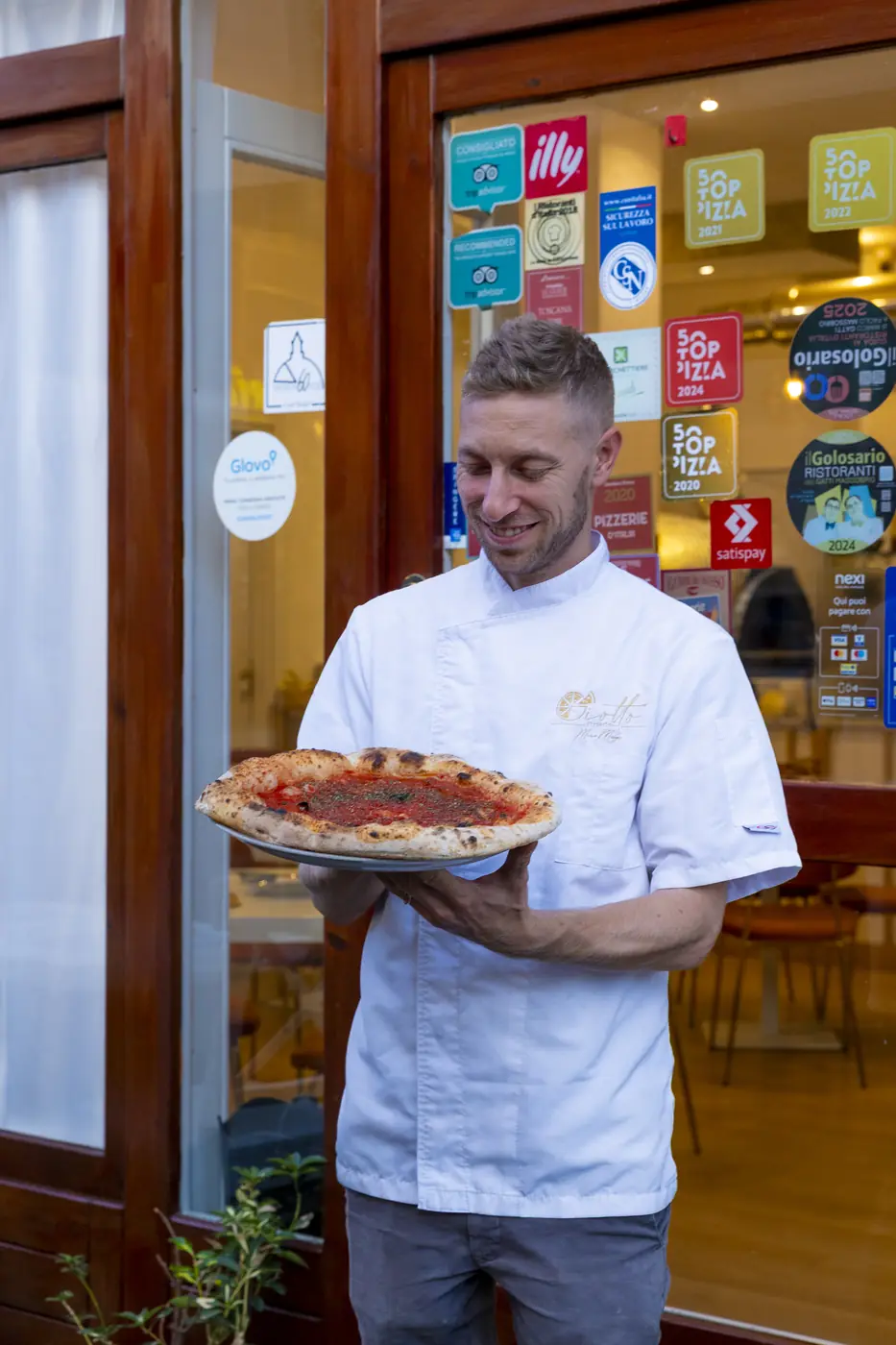 Marco Manzi all'ingresso di Giotto con una pizza, sulla vetrina gli adesivi delle guide